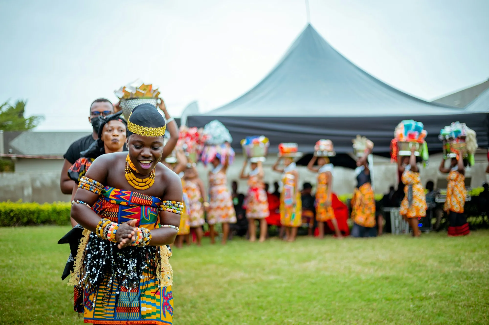 Danseuse en tenue kente, souriante, lors d'une célébration en plein air
