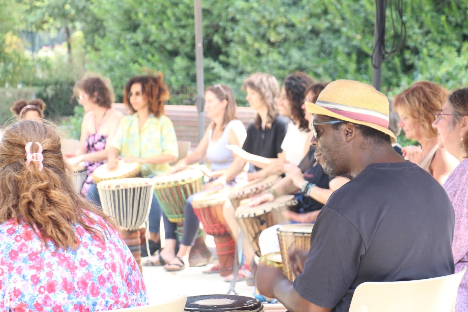 Percussionniste d'AKOFA ASBL en séance, vu de dos, groupe en mouvement en arrière-plan