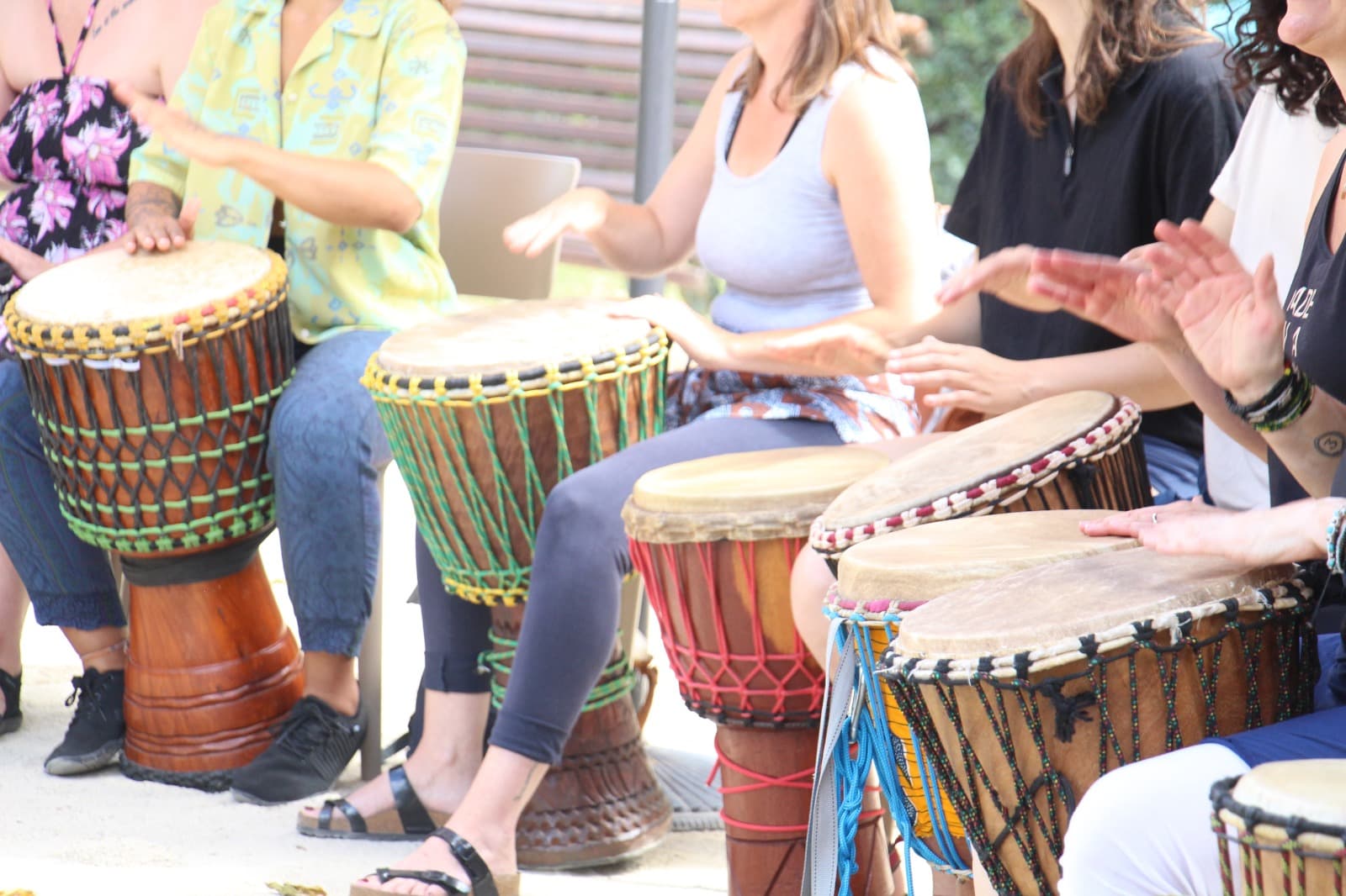 Cercle de participants assis, chacun derrière un djembé, lors d'un atelier en plein air