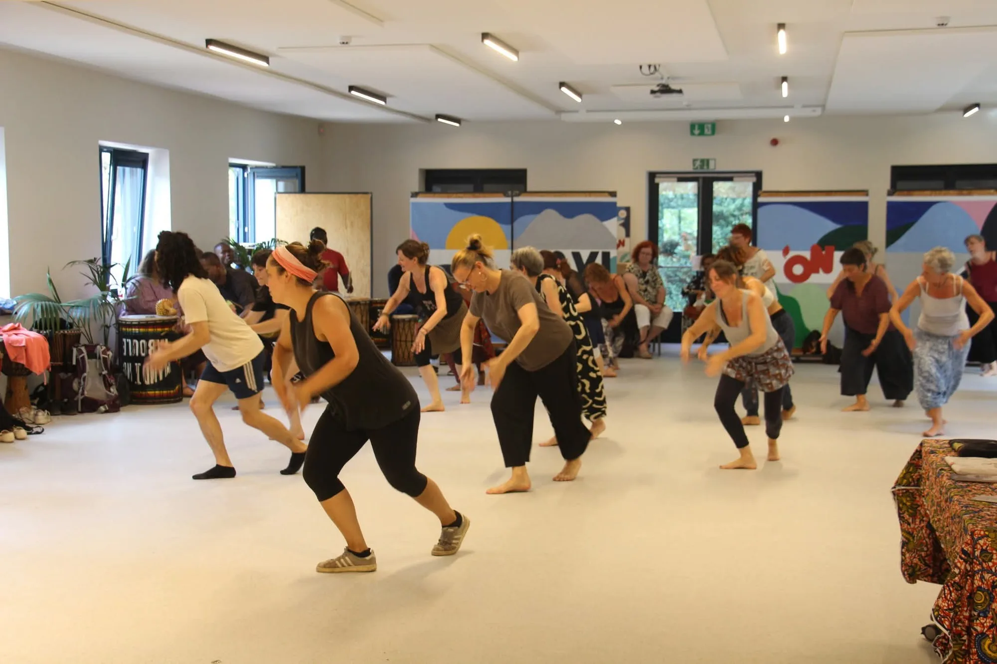 Des danseuses en plein mouvement, buste penché et jambes fléchies, dans une grande salle claire.
