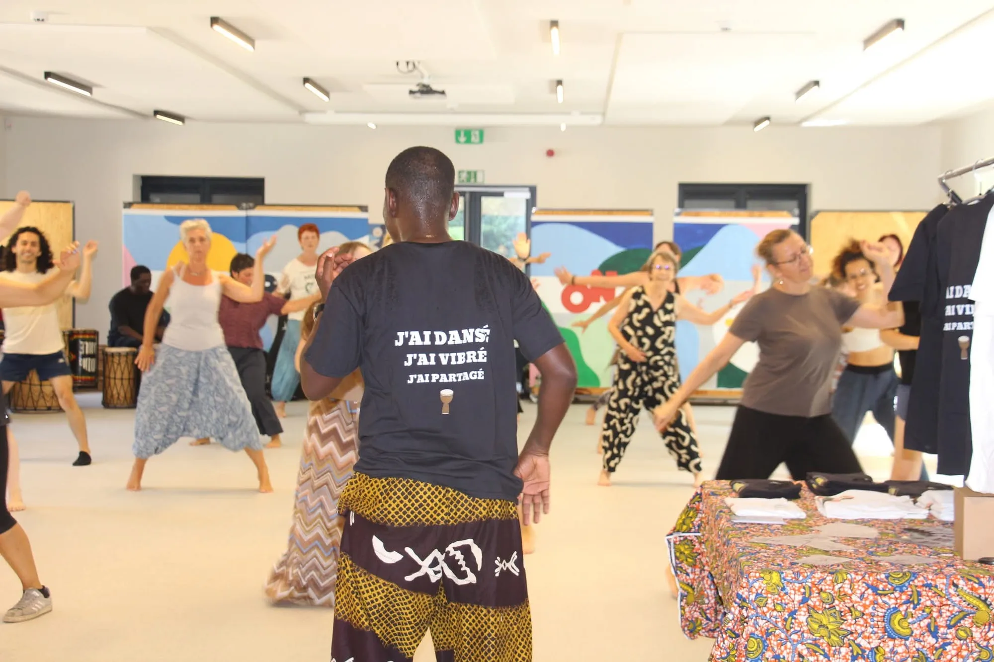 Un participant vu de dos porte un t-shirt où on lit « J'ai dansé, j'ai vibré, j'ai partagé » ; devant lui, le groupe danse.
