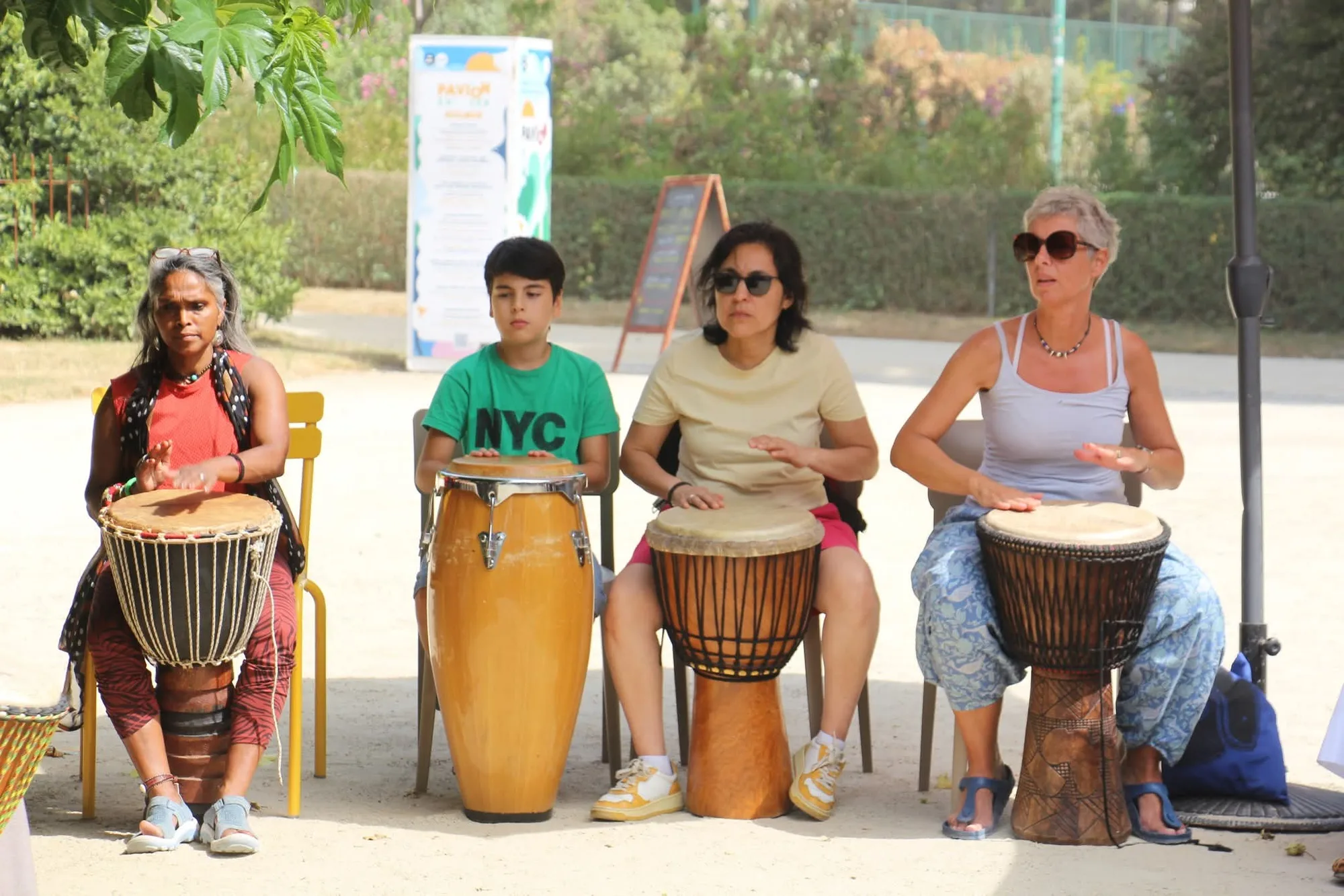 Quatre personnes jouent des percussions en extérieur ; un adolescent joue de la conga aux côtés de trois participantes au djembé.