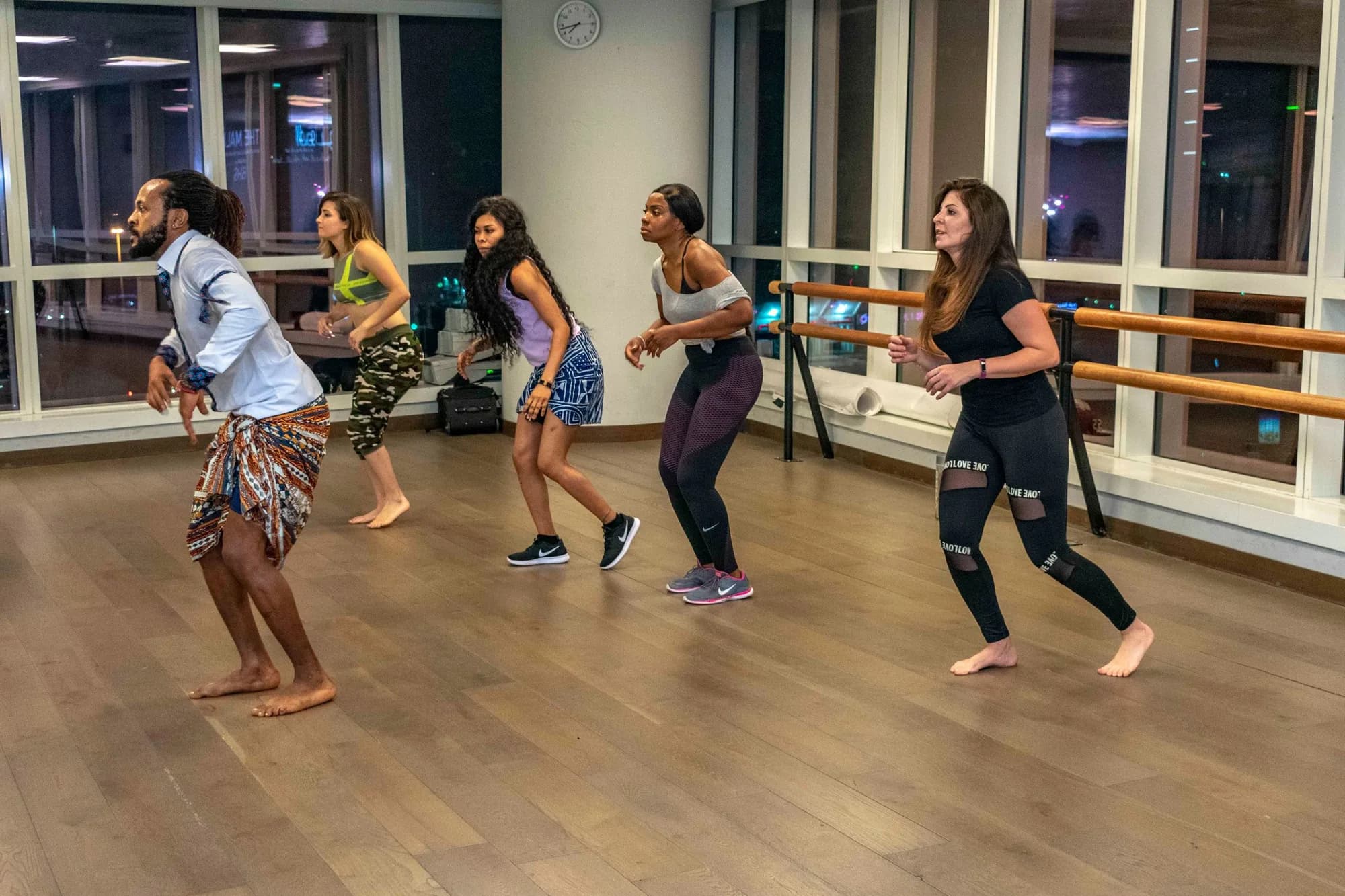 Cours de danse africaine : un groupe d'adultes suit une danseuse pieds nus en pagne, dans un studio en soirée